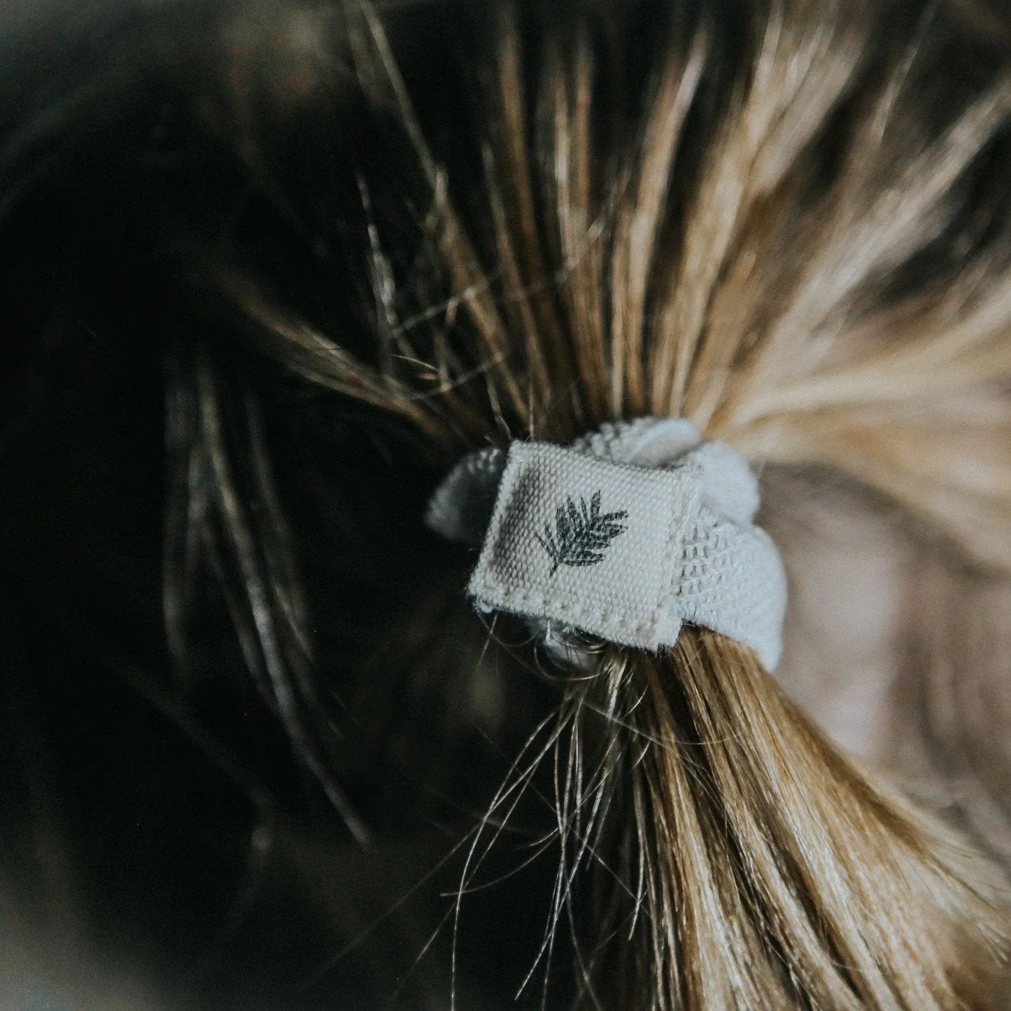 Close-up of blonde hair tied with a fabric hair tie featuring a leaf patch, Yellow B accessories