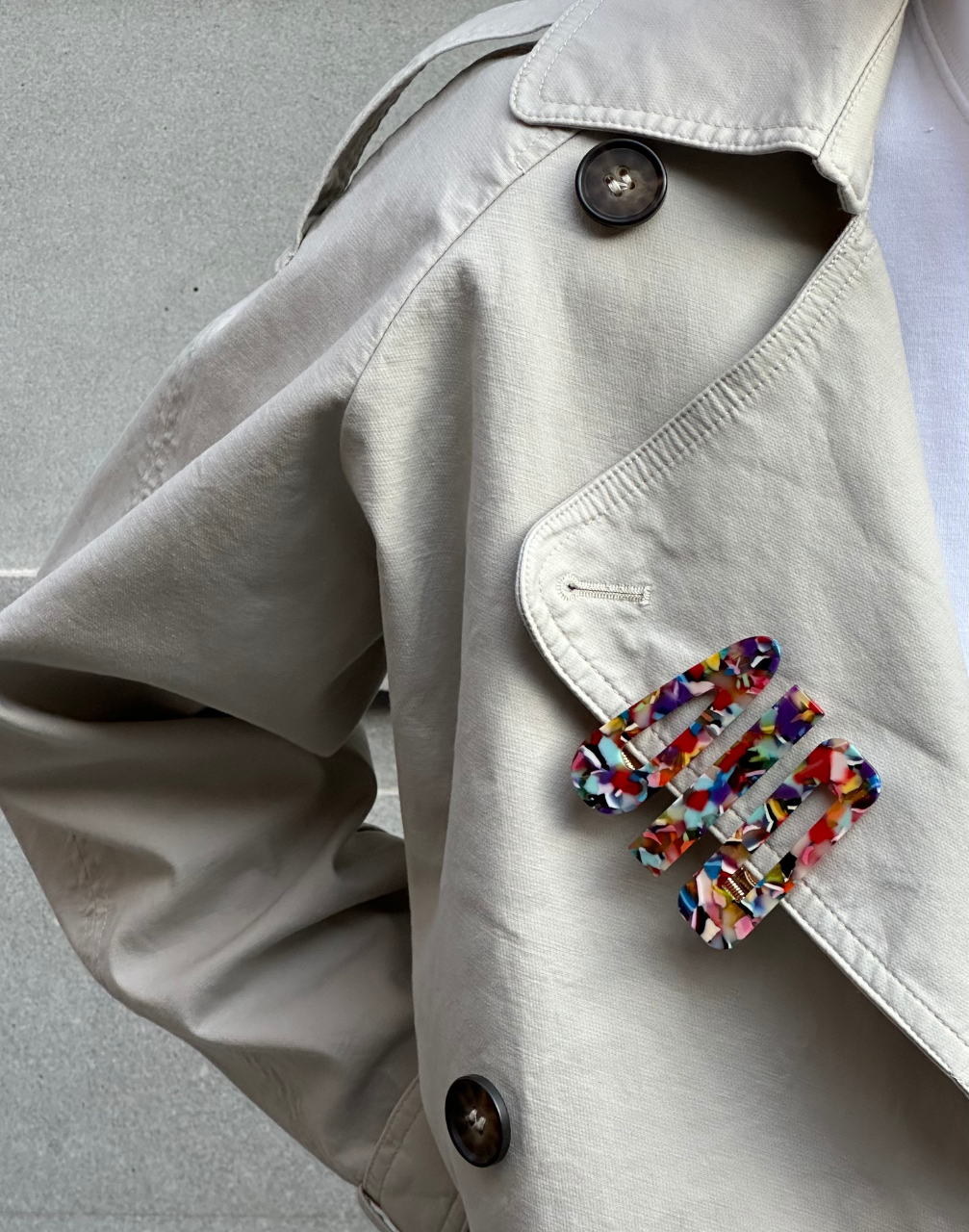 A set of three multicolour hairclips attached to a beige anorak lapel against a neutral background
