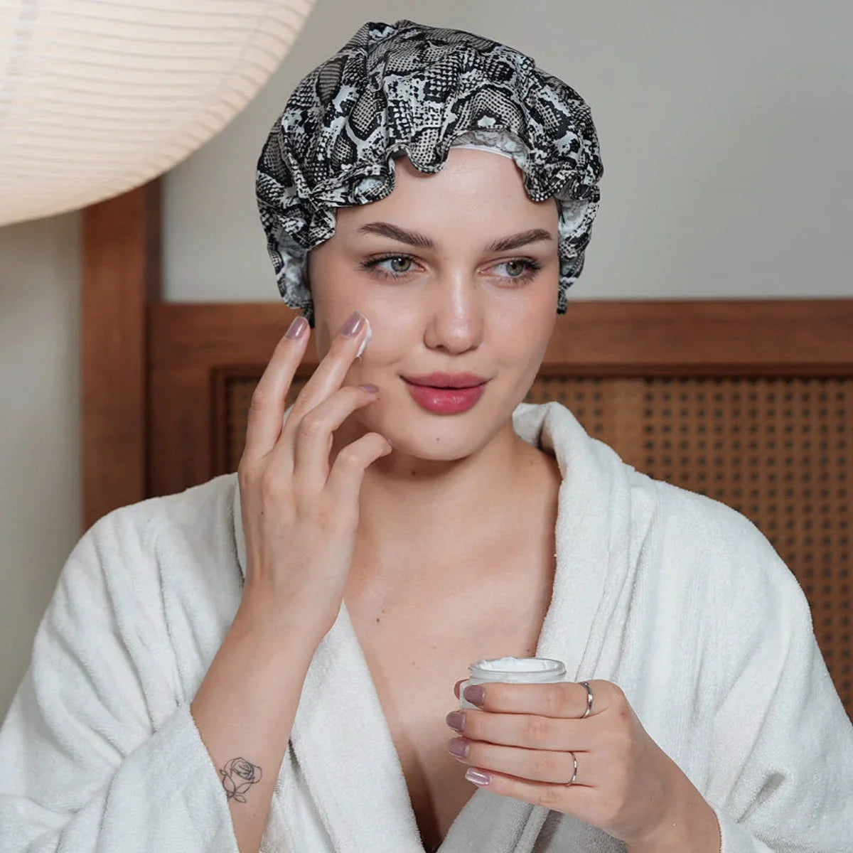Woman in robe with snake print shower cap applies face cream, highlighting Yellow B hair accessories style.