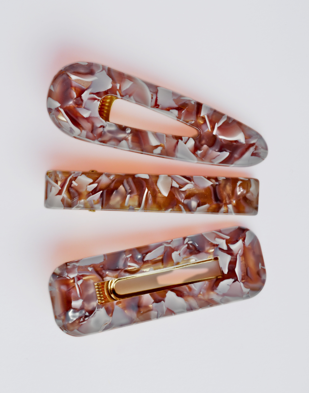 Set of three tortoiseshell patterned hair clips with gold hardware on a light grey background.