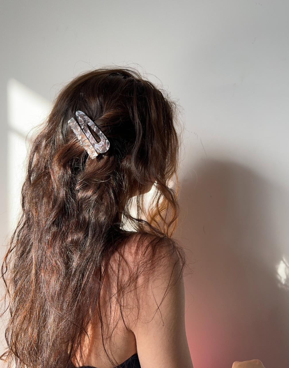 Woman with wavy hair wearing a decorative hairclip against a neutral background