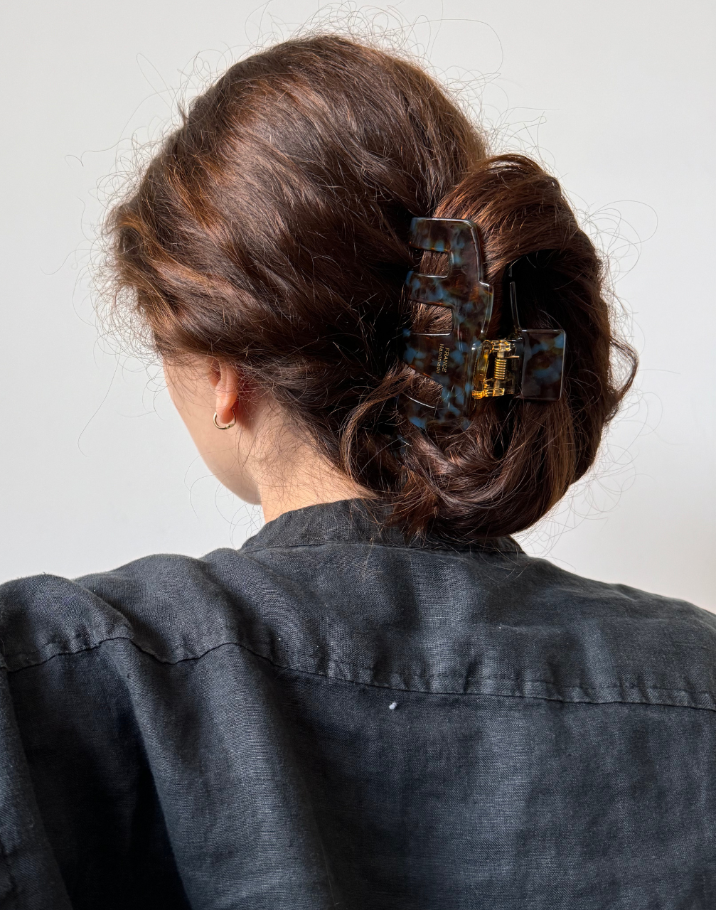 Woman with hair in a bun held in place with a brown hair claw clip against a plain background