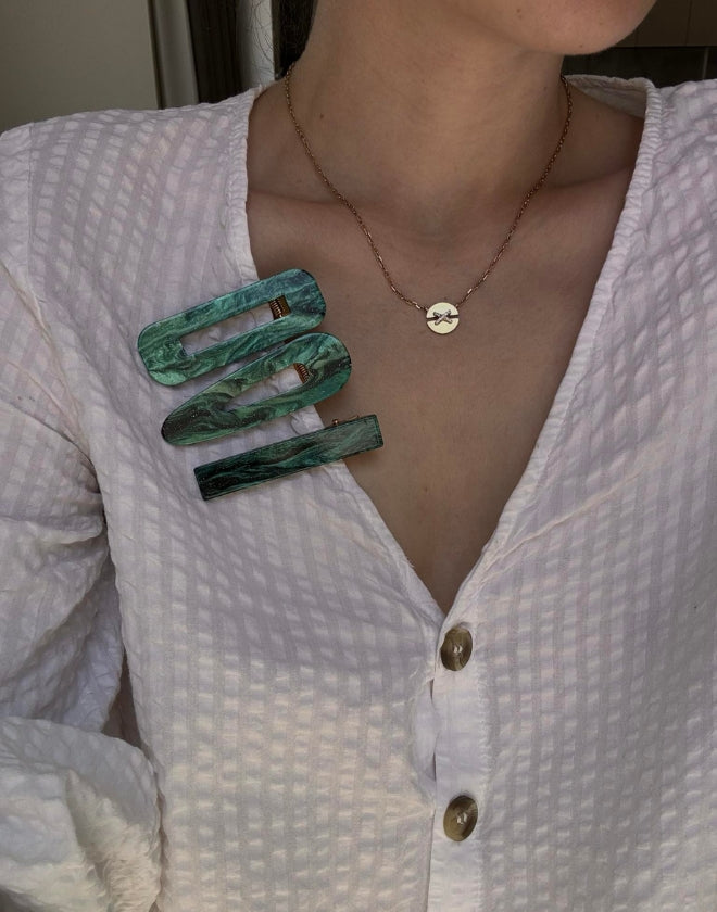 Woman wearing a set of three green hairclips attached to a textured white shirt