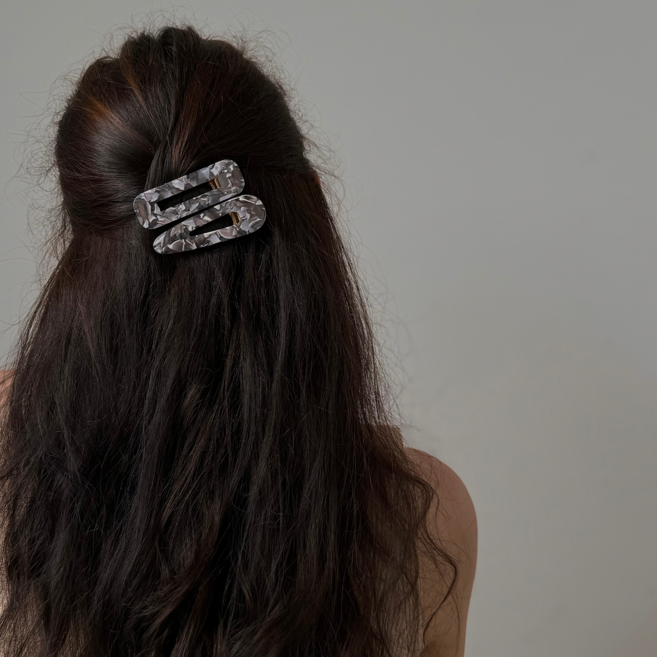 Woman with long dark hair wearing a decorative hairclip against a neutral background