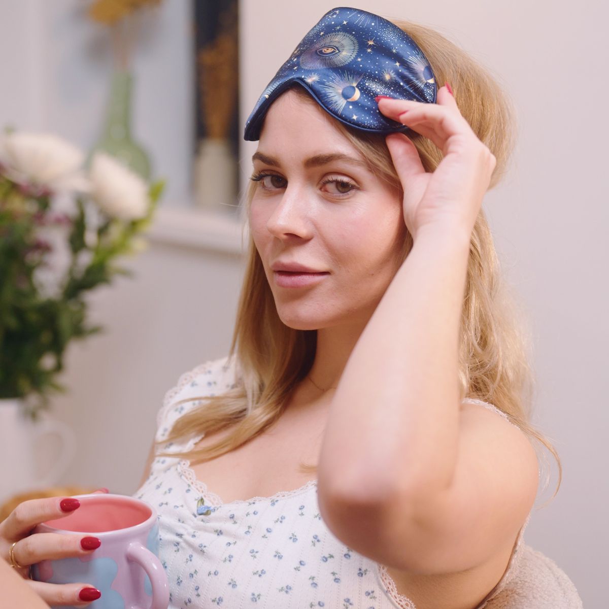 Woman wearing a SMUG starry night celestial sleep mask and holding a mug indoors.