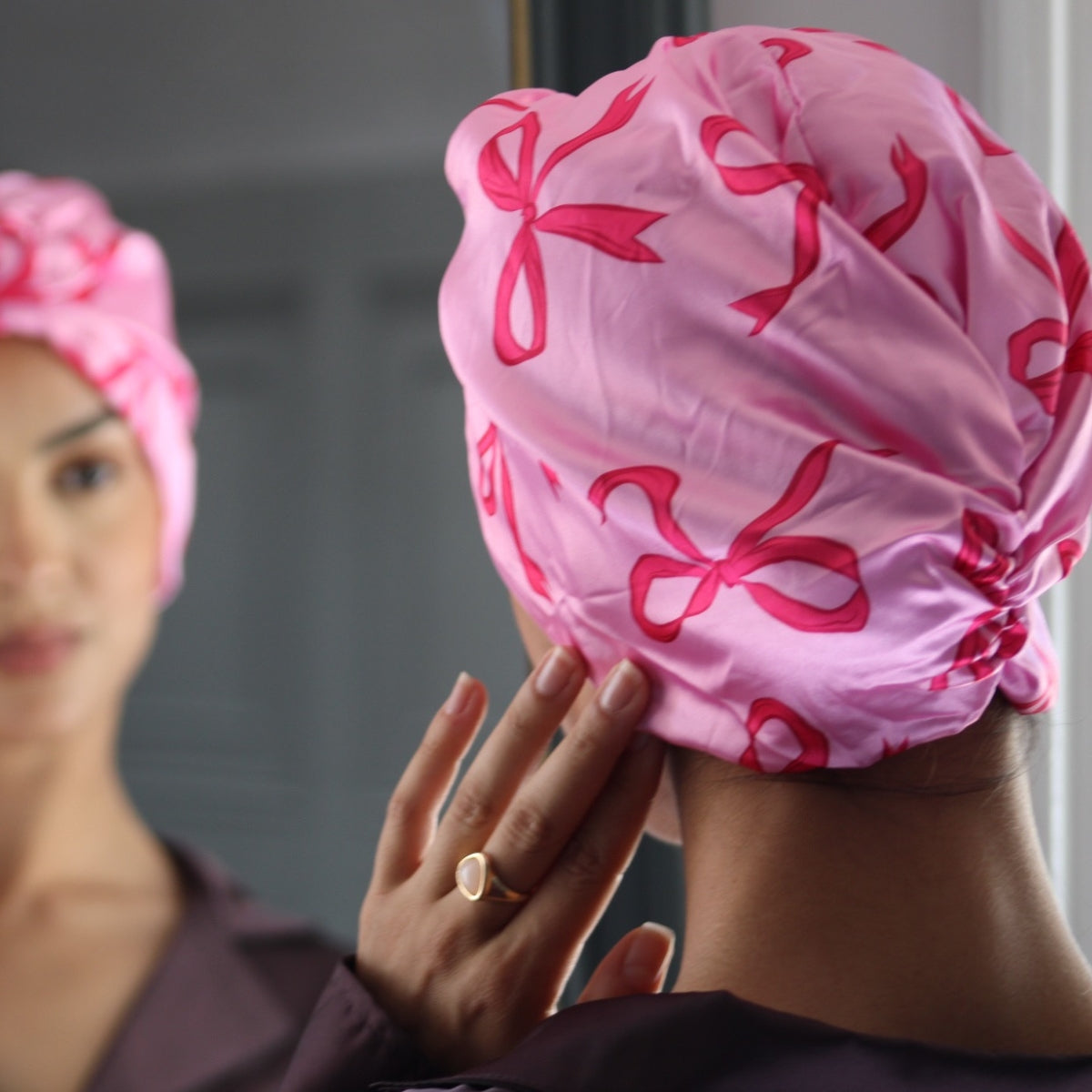 Person wearing a SMUG Pink Bows Patterned Satin Sleep Turban, in front of a mirror.