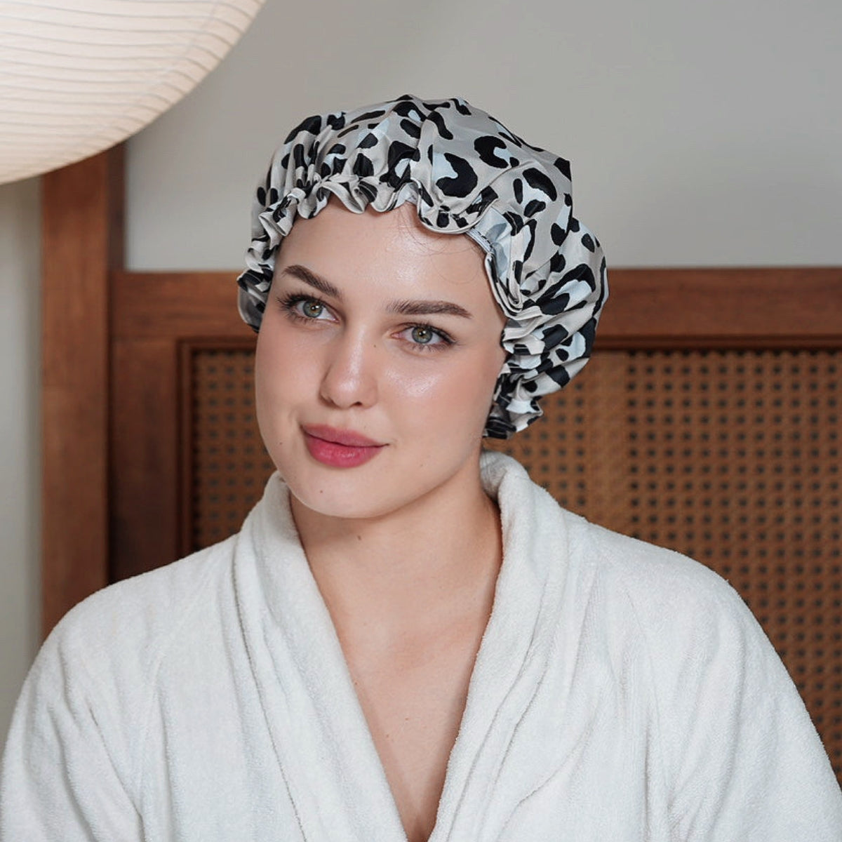 Woman wearing a SMUG leopard print shower cap indoors.
