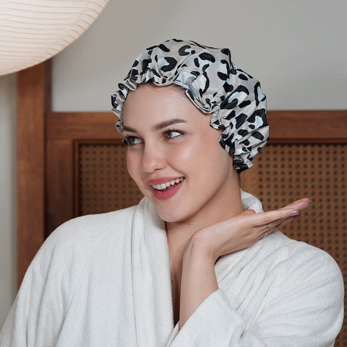 Woman wearing a SMUG leopard print shower cap in a bedroom.