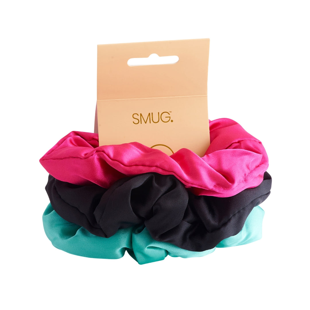 Three scrunchies in aqua, pink and black with a 'SMUG' brand card on a white background
