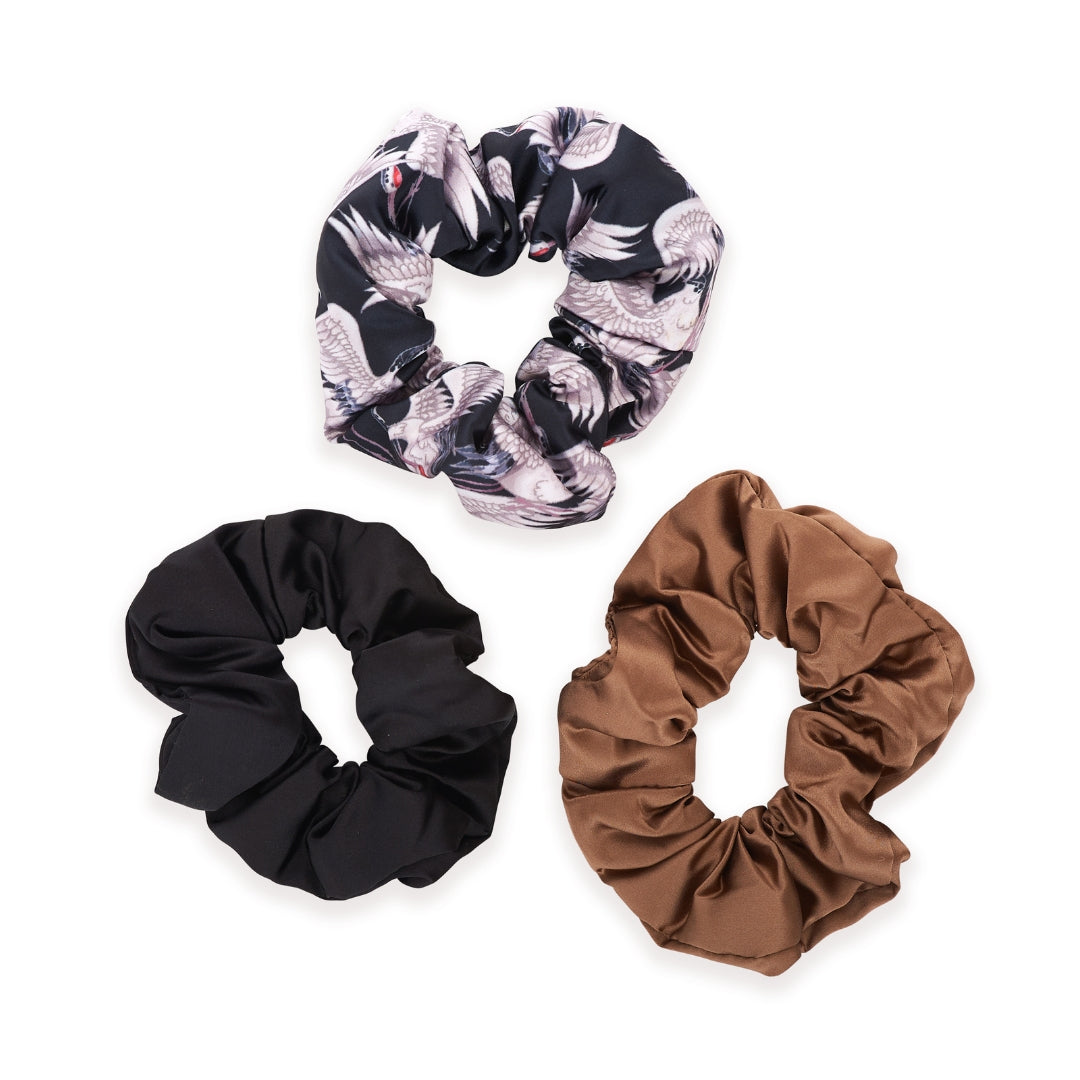 Three scrunchies in an elegant crane-printed design, sumptuous mocha satin and timeless black on a white background