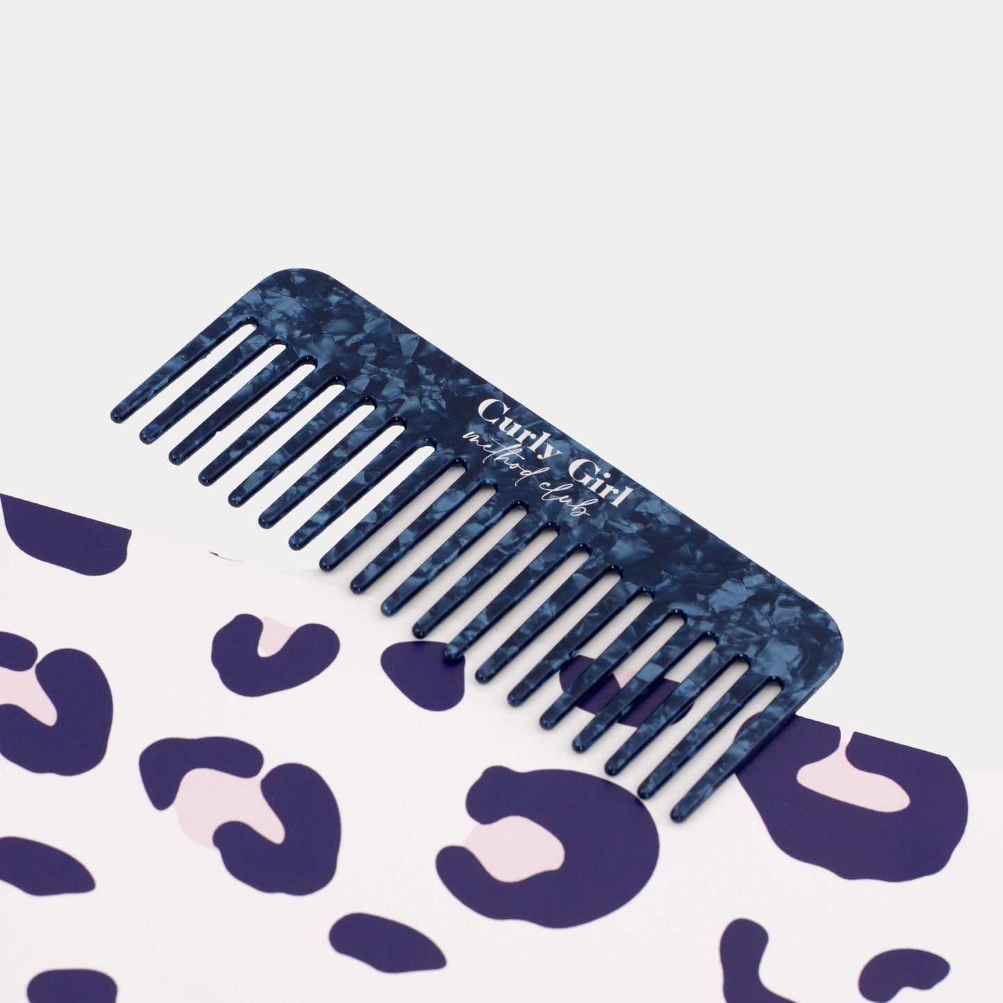 Blue marbled comb with 'Curly Girl Method Club' text on a light purple background with abstract shapes