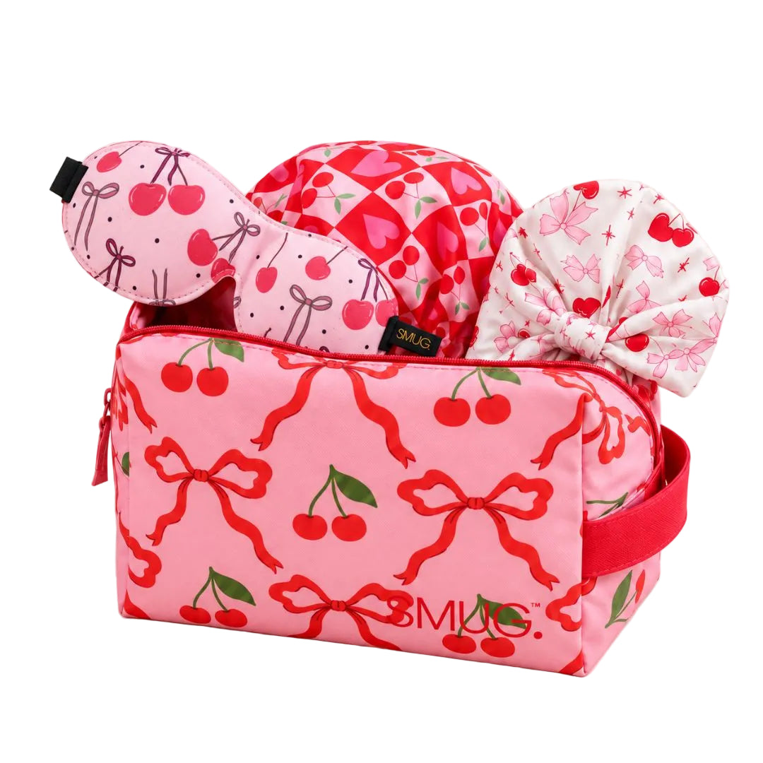SMUG cherry-print wash bag holding a pink sleep mask, shower cap and satin sleep turban.